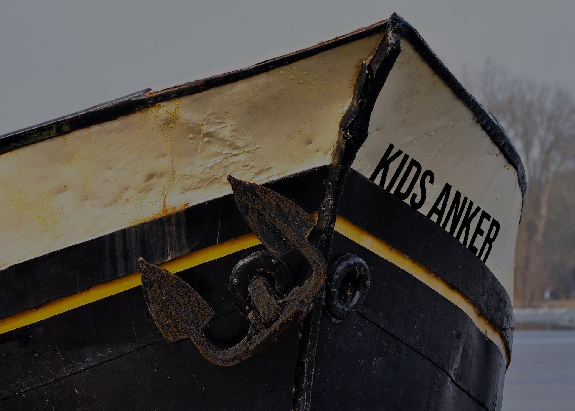 Der Bug eines Schiffes ist zu sehen, an dem ein Anker hängt. Auf dem Boot steht „Kids Anker