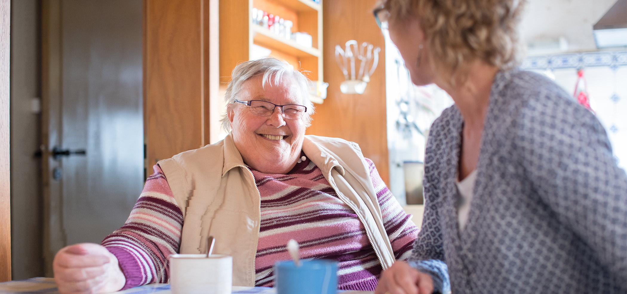 Ältere Dame lächelt in die Kamera, im Vordergrund die Silhouette einer anderen Frau
